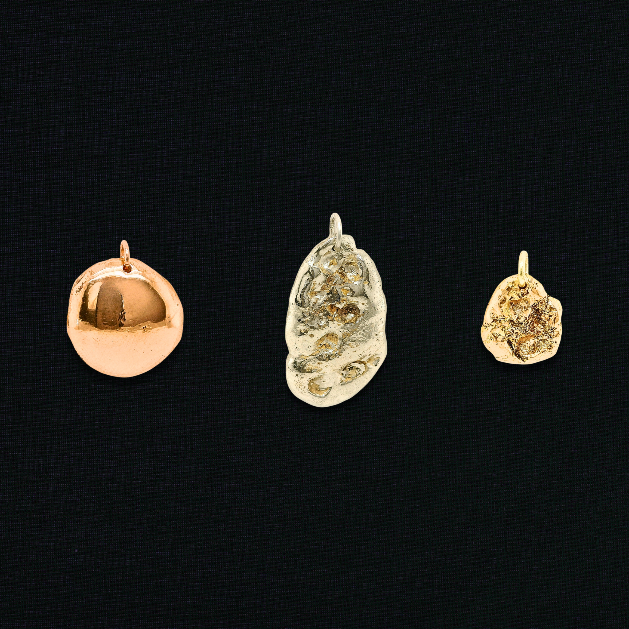 Drei Re-Loved Liminoko Nugget-Anhänger aus Weißgold, Roségold und Gelbgold, luxuriös und einzigartig handgefertigt aus recyceltem Schmuck, nebeneinander auf schwarzem Stoffhintergrund.