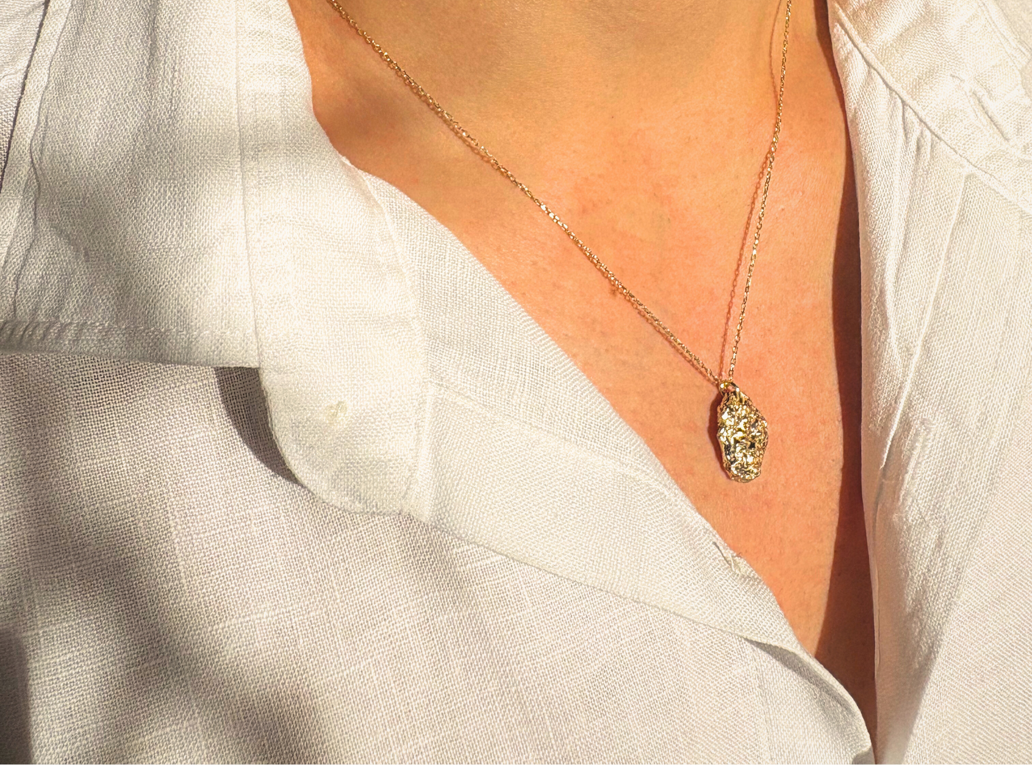 Liminoko Nugget-Anhänger aus recyceltem Gold, handgefertigt aus geerbten Schmuckstücken, getragen zu weißem Leinenhemd.