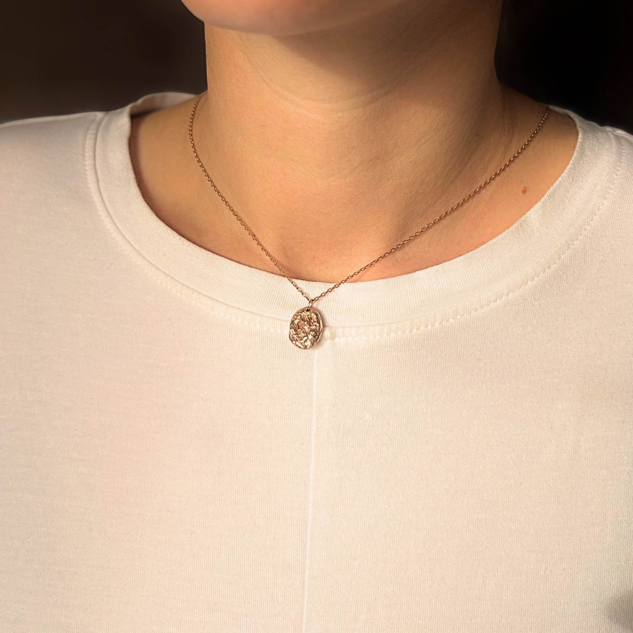 Liminoko Nugget-Anhänger aus recyceltem Gold, handgefertigt, getragen zu schlichtem weißen Shirt im warmen Licht.