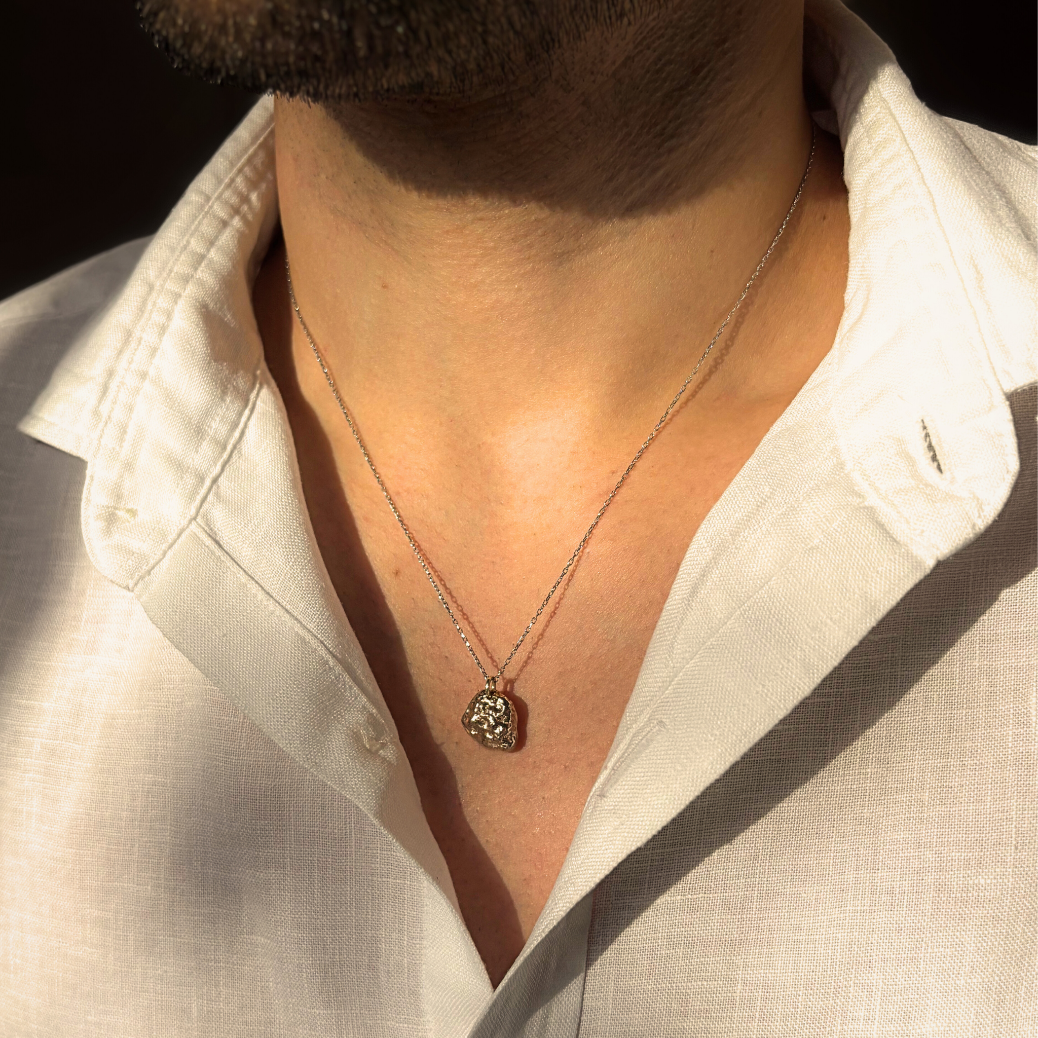 Liminoko Nugget-Anhänger aus recyceltem Gold in Weißgold mit Gelbgold Akzenten handgefertigt, getragen zu offenem weißen Hemd im warmen Licht.