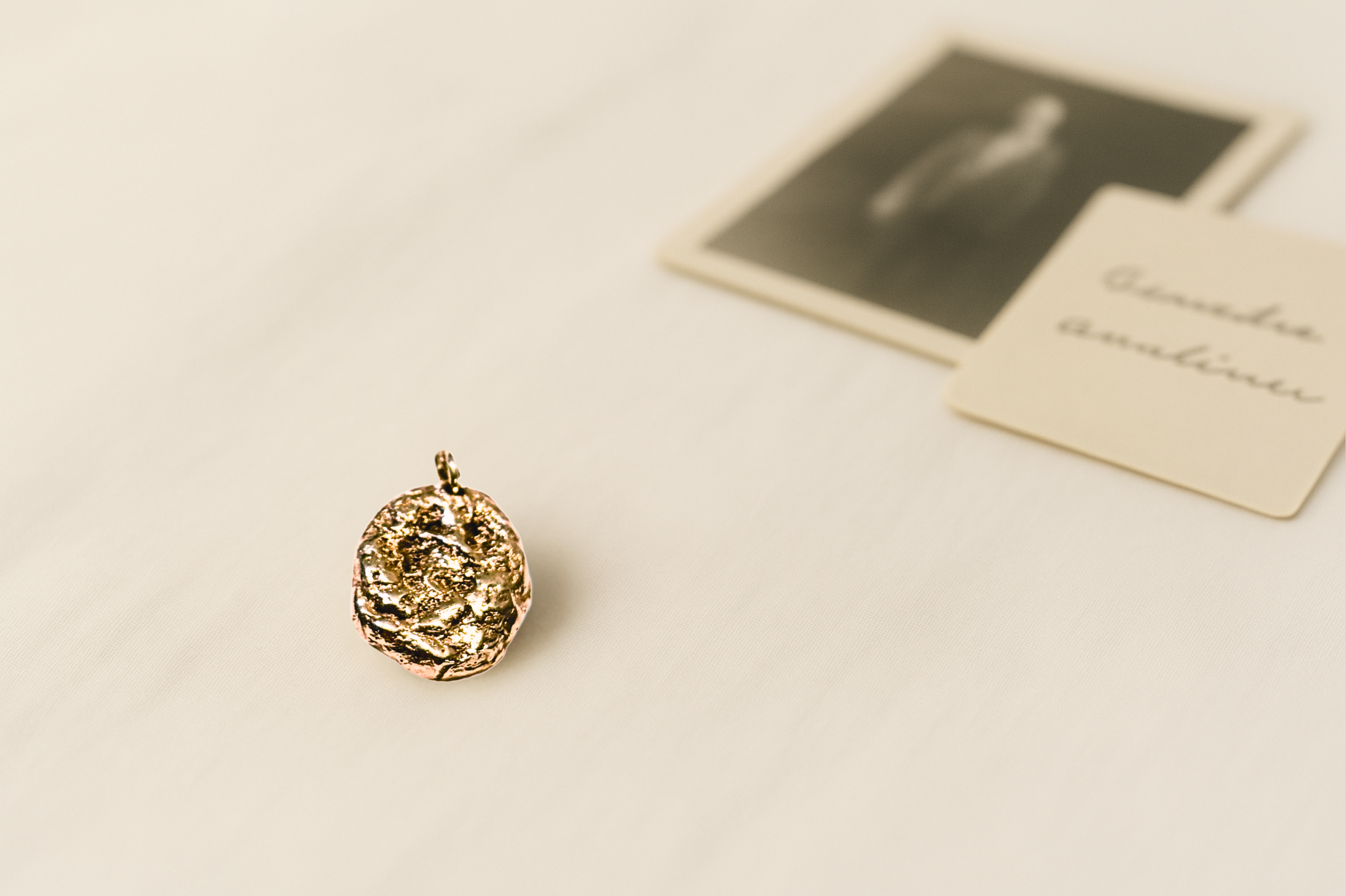 Liminoko Nugget-Anhänger aus recyceltem Gold, handgefertigt aus geerbten Schmuckstücken, auf hellem Stoff mit Vintage-Foto im Hintergrund.